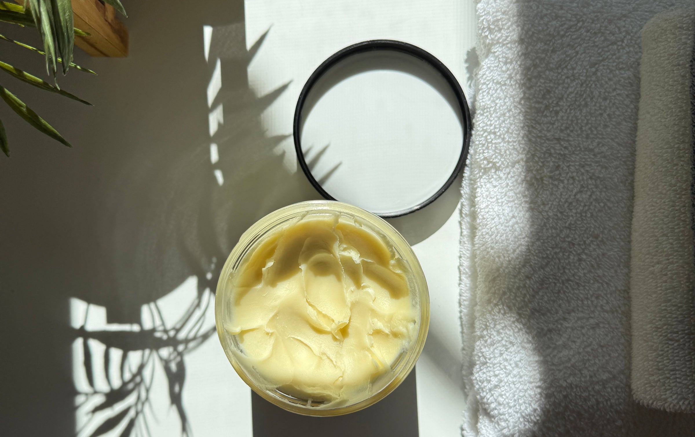 Jar of sanoun shea butter on a towel with a plant shadow